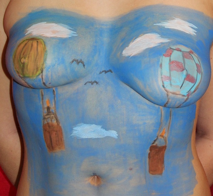 painting on female torso of two hot air balloons in the sky among clouds and birds