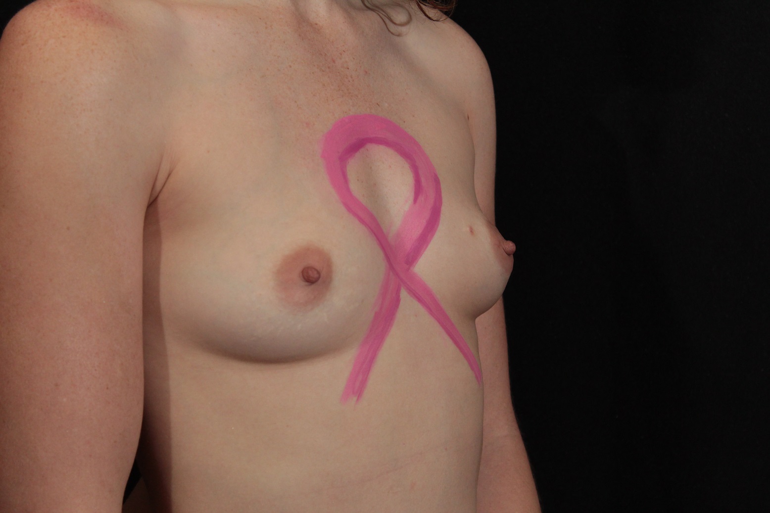 Body painting of pink ribbon on female chest.