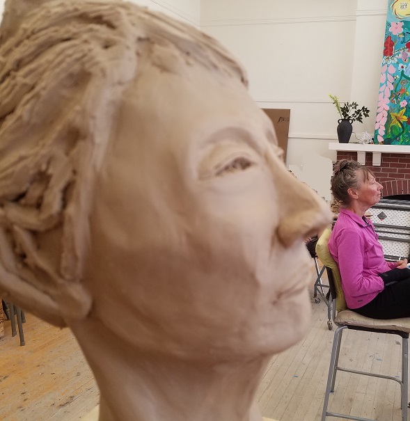 sculpture in progress of female head with actual model in background