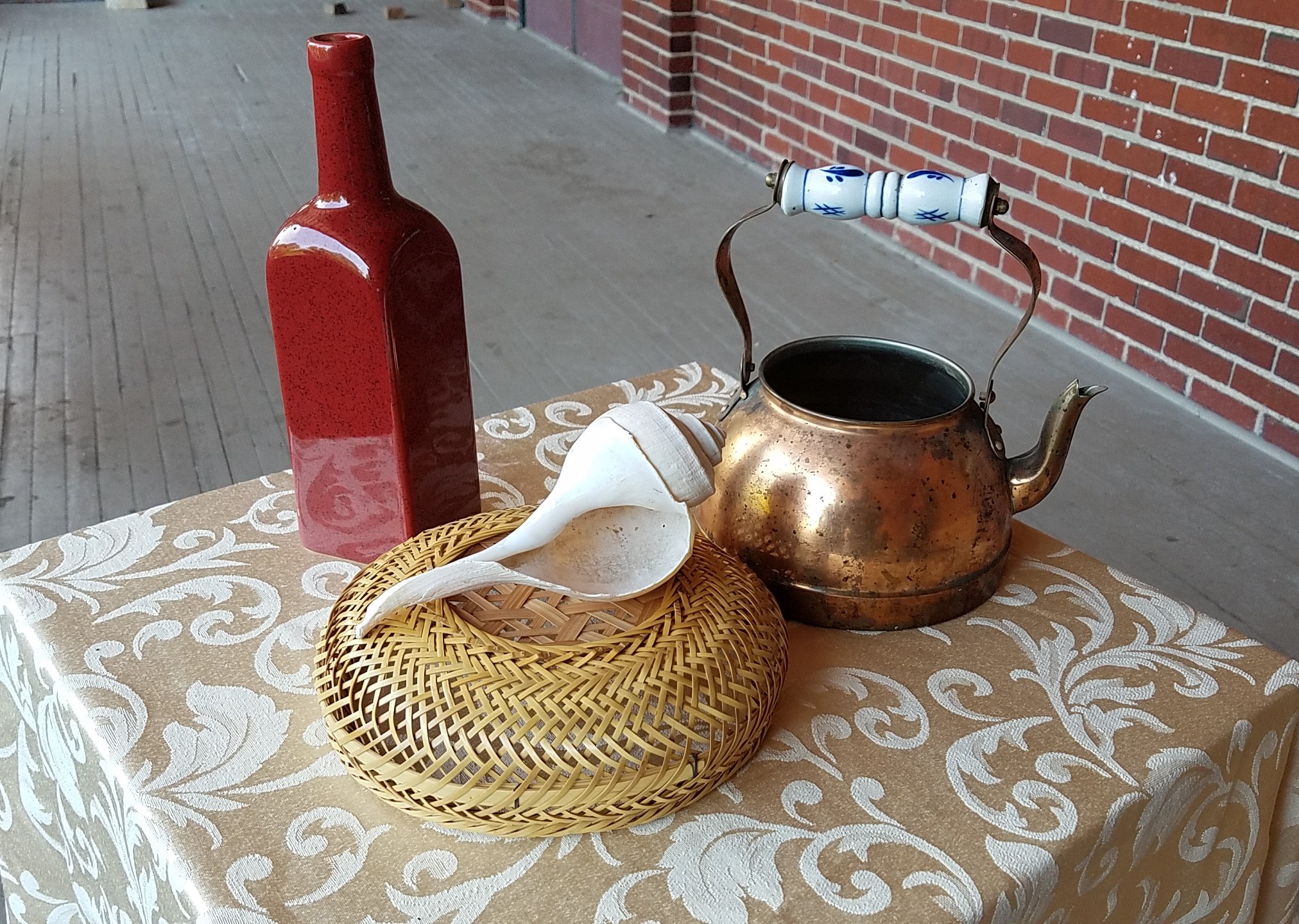 photo of red glass bottle, wicker basket and copper kettel