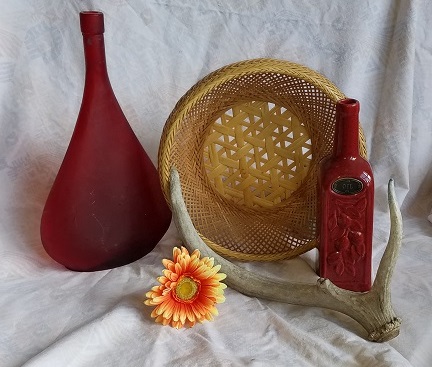 photo of two red glass bottles, wicker basket, antlers, plastic flower