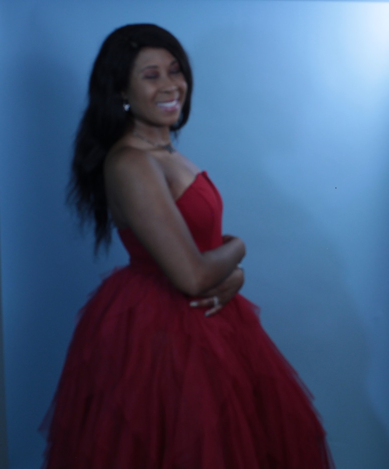 Photo of Lara, clothed, in red dress front of a blue backdrop